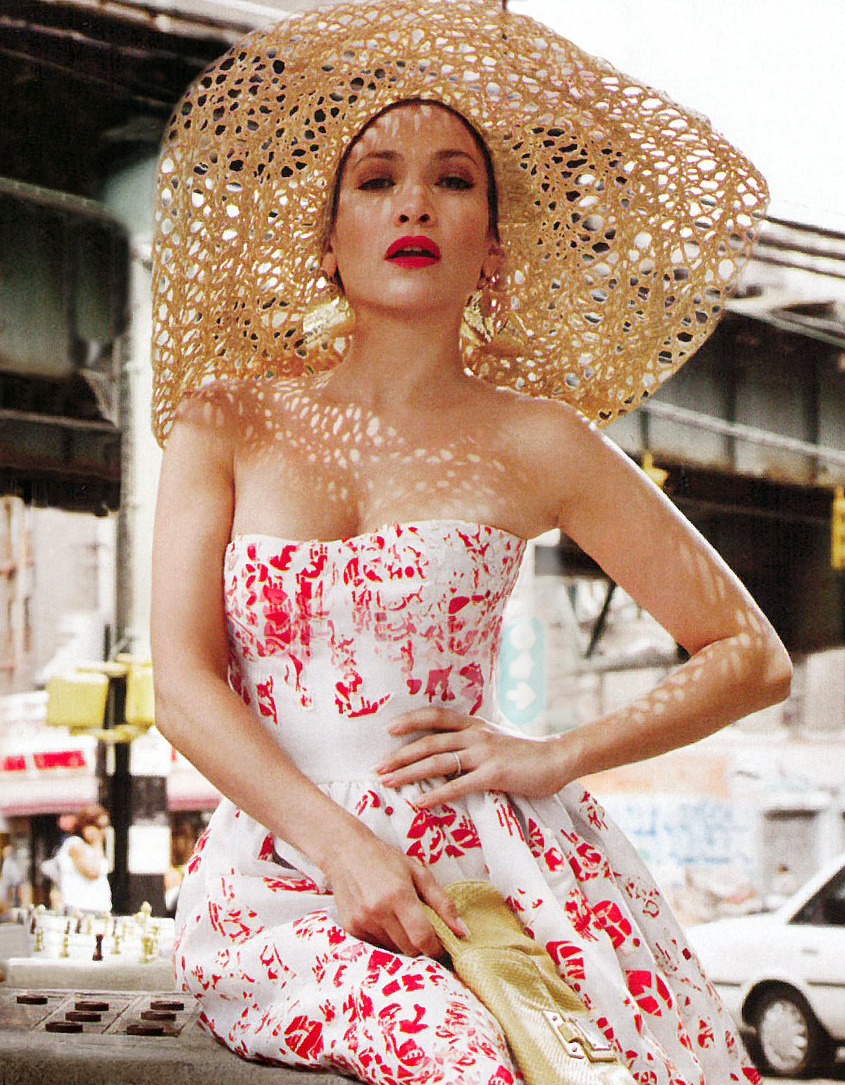 Woman wearing a large straw hat and a red and white dress in an urban setting.