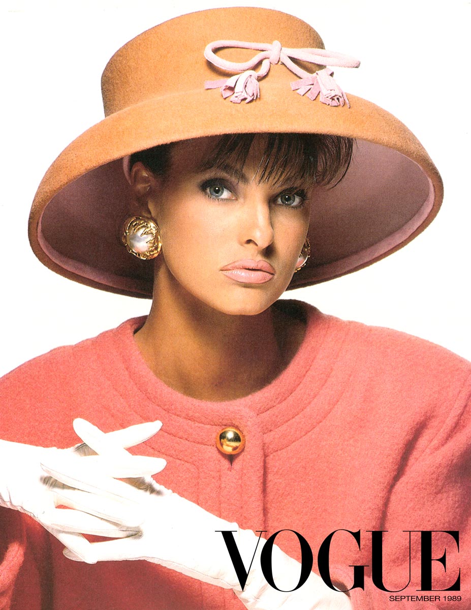 Woman wearing a large beige hat with a pink bow, a pink coat, and white gloves, with 'Vogue' branding.