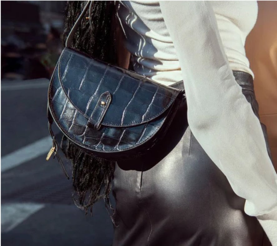Person carrying a dark blue crocodile-patterned handbag in urban setting.