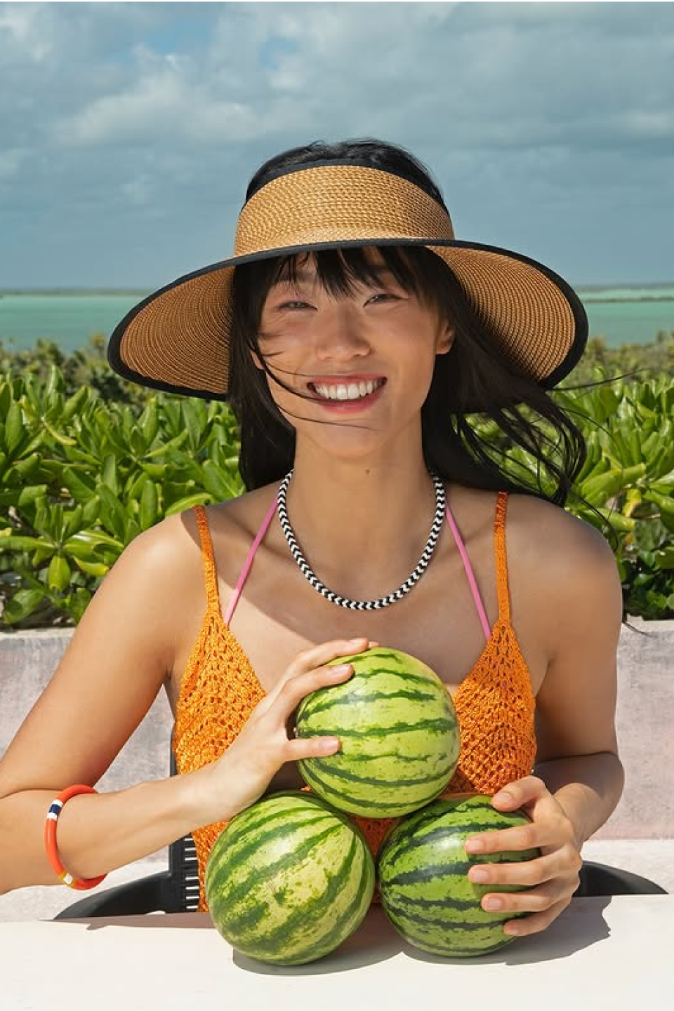 Smiling woman in sunhat holding three small watermelons outdoors.