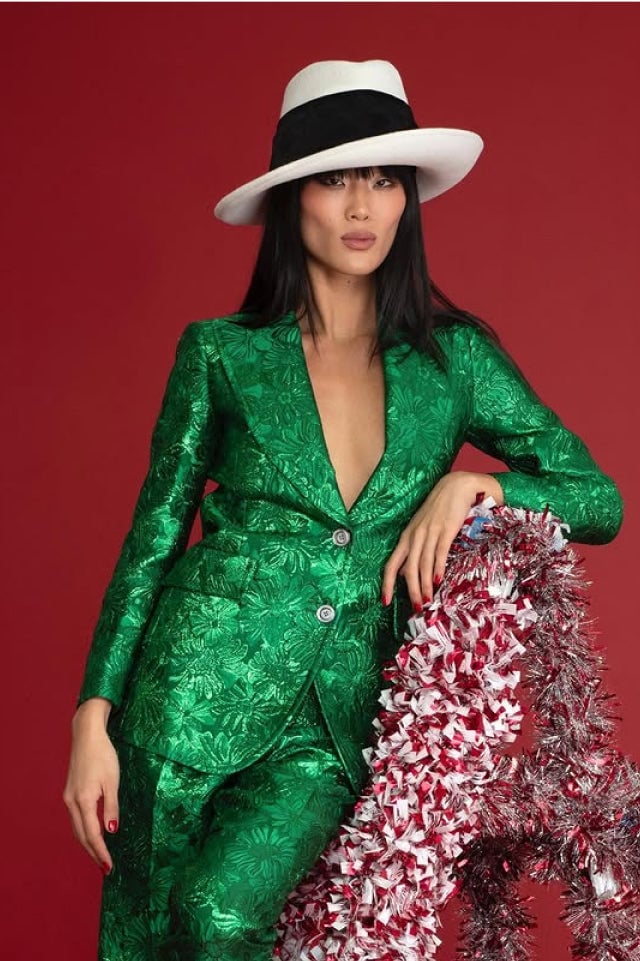 Person in a green suit and white hat, leaning on tinsel against a red background.