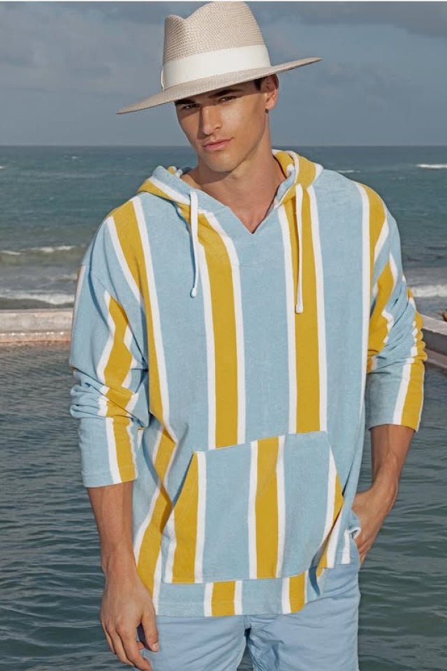 Man in striped hoodie and hat by the ocean.